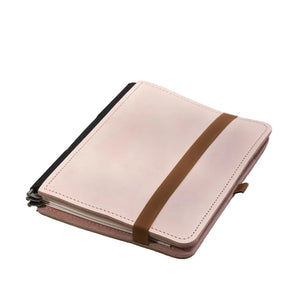 A light pink leather notebook cover with a brown elastic band closure, shown on a neutral light gray background.