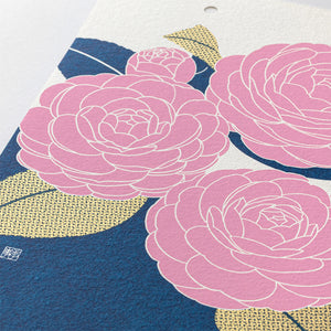 A close-up of a textured paper print featuring stylized pink flowers with white outlines, navy blue background areas, and textured gold leaf-like shapes.