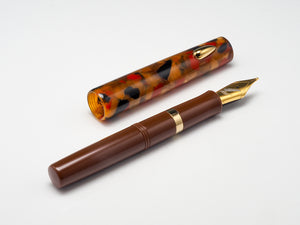 A brown fountain pen with a gold nib and trim, shown next to its matching tortoiseshell-patterned cap on a clean white background.