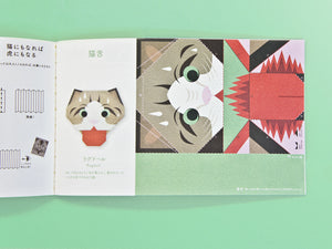 An open Japanese origami book on a mint green background, showing a cat-themed folding craft with illustrated and folded paper panels.
