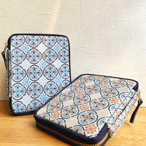 Two zippered pouches with a blue, beige, and brown geometric tile pattern, displayed on a wooden surface against a light textured wall.