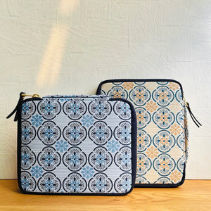Two zippered pouches with a blue, beige, and black geometric medallion pattern, displayed on a wooden surface against a light textured wall.