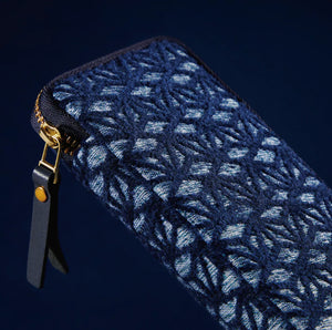 A close-up of a dark navy blue zippered pouch featuring a textured, woven Japanese wave pattern in lighter blue and white threads, with a black leather pull tab and gold-tone hardware.