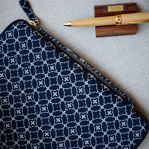 Navy blue pouch with white geometric pattern, gold pen, and wooden box on gray surface