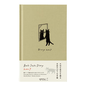 A Beako Style Diary 2017 with a light olive green cover featuring a black cat illustration in a mirror, and a white lower section with product text and a cat silhouette.