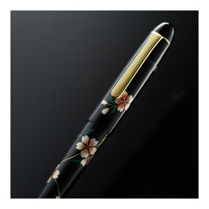 A luxury black fountain pen with an elegant gold clip and gold trim, decorated with delicate cherry blossom floral engravings, shown diagonally on a dark gradient background.