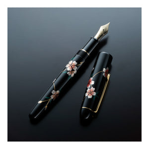 A black fountain pen and matching cap with hand-painted cherry blossom motifs, displayed on a dark reflective surface.