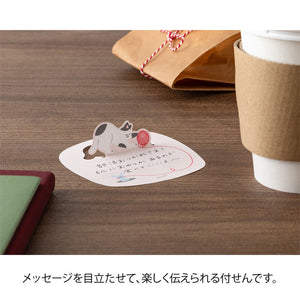 Card with a cat illustration on a wooden surface with a cup and gift box.