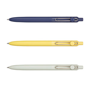 Three retractable ballpoint pens shown horizontally on a white background, in navy blue, pale yellow, and off-white. Each pen has a metal clip and a small circular logo badge on the cap.