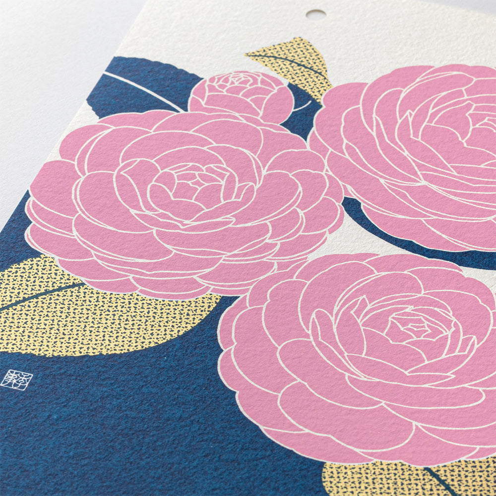 A close-up of a textured paper print featuring stylized pink flowers with white outlines, navy blue background areas, and textured gold leaf-like shapes.