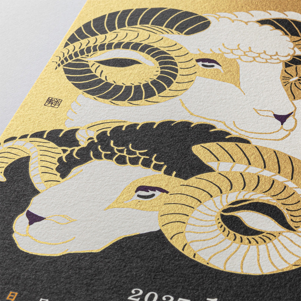 Close-up of a Japanese-style art print featuring two ram heads with large curled horns in gold, black, and off-white, with part of a dark textured surface and small white numerals visible below.