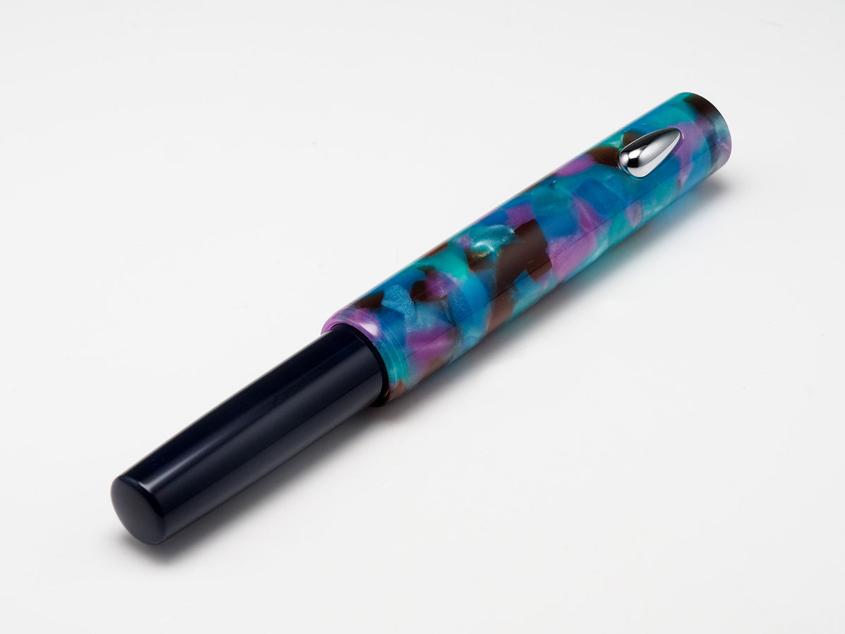 A marbled resin pen with a vibrant blue, purple, and green pattern, paired with a solid black cap, shown on a clean white background.