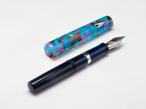 A fountain pen and its cap displayed on a clean white background. The pen body is dark navy blue with a silver band, and the cap features a marbled pattern of blue, purple, and brown.