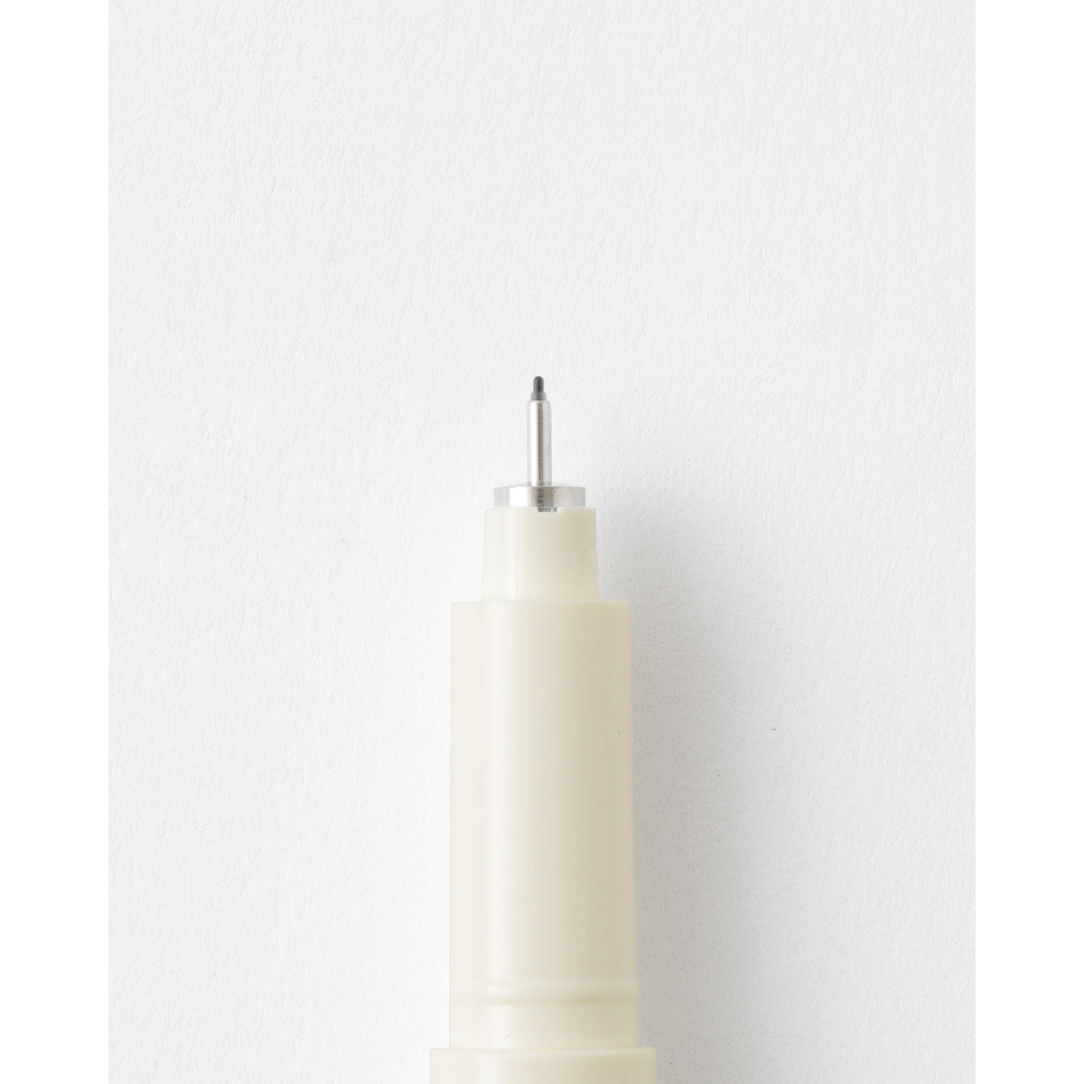 Close-up of a cream-colored marker or pen tip with a silver metal needle, set against a clean white background.