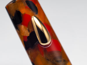 Close-up of a glossy tortoiseshell-style pen body with amber, black, and red marbling, featuring a polished gold clip on a light gray background.
