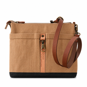 A structured canvas shoulder bag in tan with brown leather straps and a black base, featuring a vertical zippered pocket 