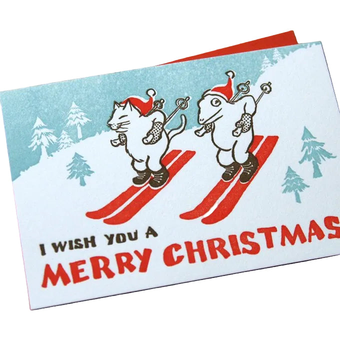 Christmas card with skiers and 'I wish you a Merry Christmas' text on a wooden surface