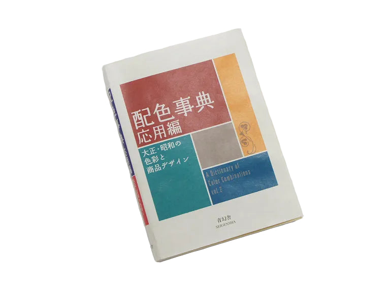 A book titled '配色事典 応用編' (Dictionary of Color Combinations Volume 1) resting on a plain white surface. The cover features a geometric color block design with red, orange, teal, blue, and gray sections on an off-white background.