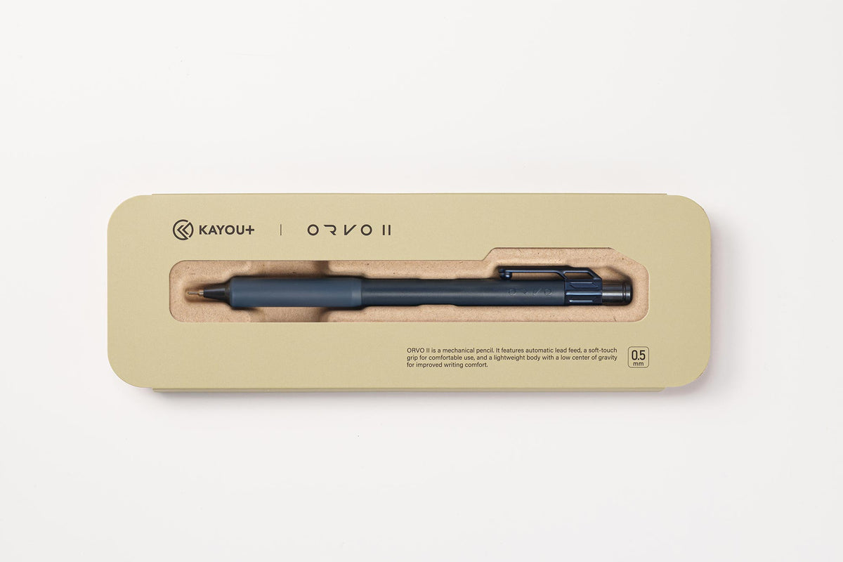 A KAYOU+ ORVO II ballpoint pen in a dark blue-gray color, presented inside its beige cardboard packaging with a clear window.
