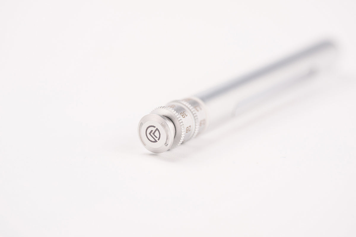 A close-up of a silver metal pen tip with a textured adjustment ring and a circular logo emblem, set against a clean white background.