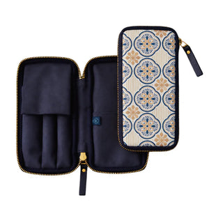 A zip-around organizer case shown open and closed on a white background. The exterior has a cream base with a blue and tan geometric medallion pattern, while the interior is dark navy with gold-tone zippers and a small blue brand tab.