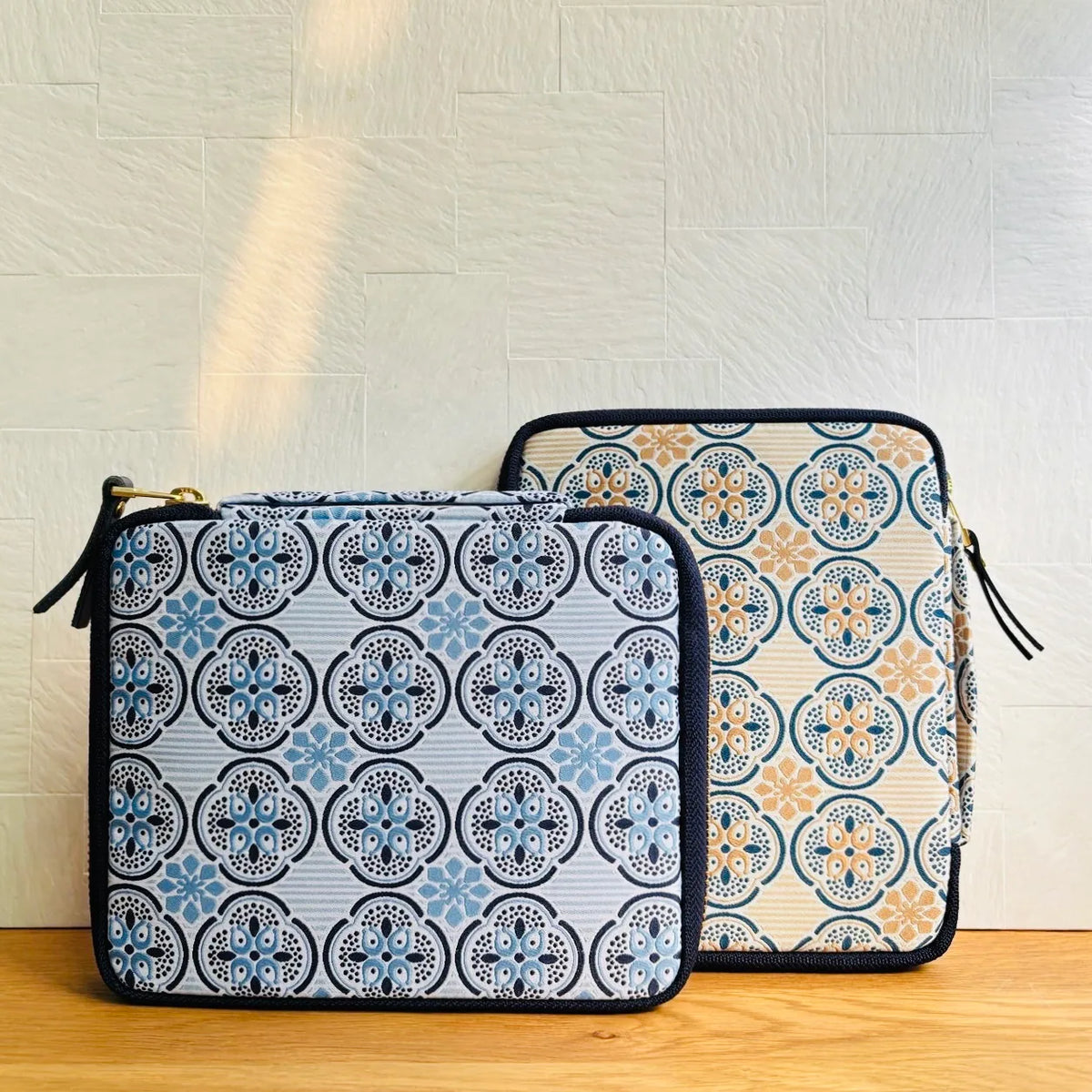 Two zippered pouches with a blue, beige, and black geometric medallion pattern, displayed on a wooden surface against a light textured wall.