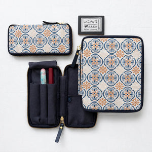 Three views of a zippered fabric organizer case with a blue and orange geometric medallion pattern on a cream background, shown closed and open with interior pockets and accessories, plus a small brand card on a white background.