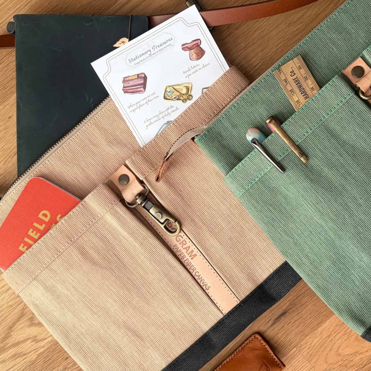A close-up flat lay of a canvas wallet organizer on a wooden surface, showing a beige front pocket with a leather zipper pull reading 'Cream Color Connoisseur,' a green side pocket with metal tools, and card slots holding a card and small items.