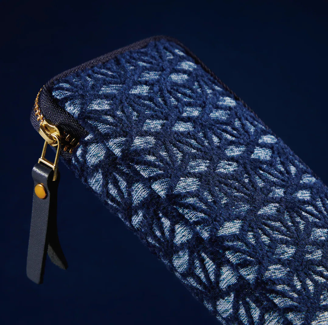 A close-up of a dark navy blue zippered pouch featuring a textured, woven Japanese wave pattern in lighter blue and white threads, with a black leather pull tab and gold-tone hardware.