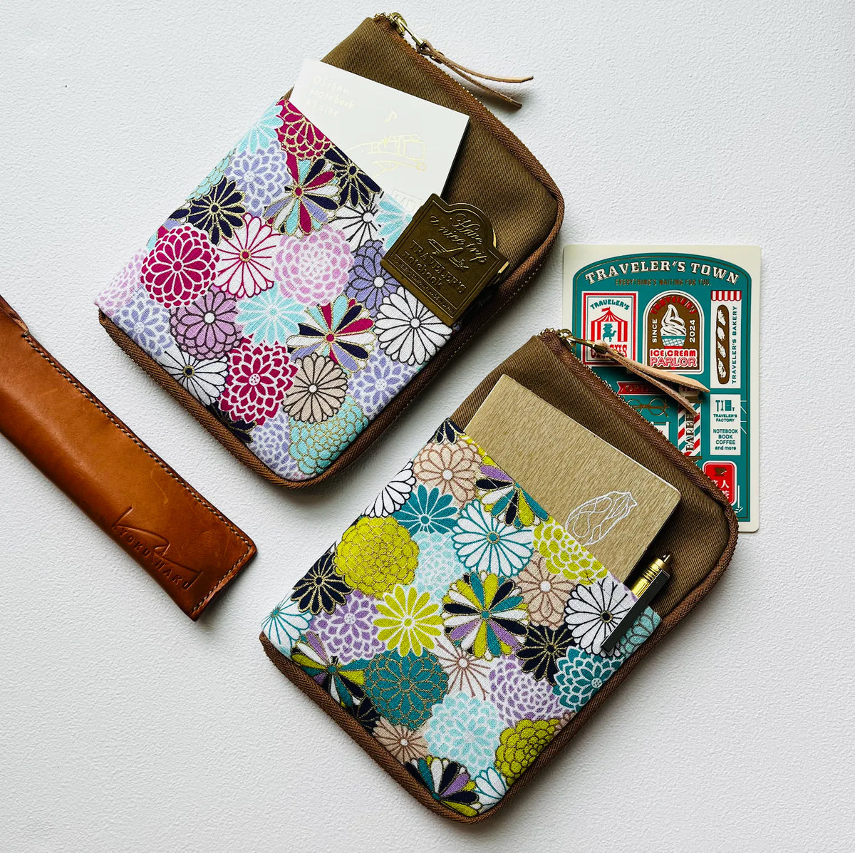 Two small zip-around card holders with brown leather trim and a colorful floral patterned fabric front, shown on a light background with inserted cards and a matching leather strap.