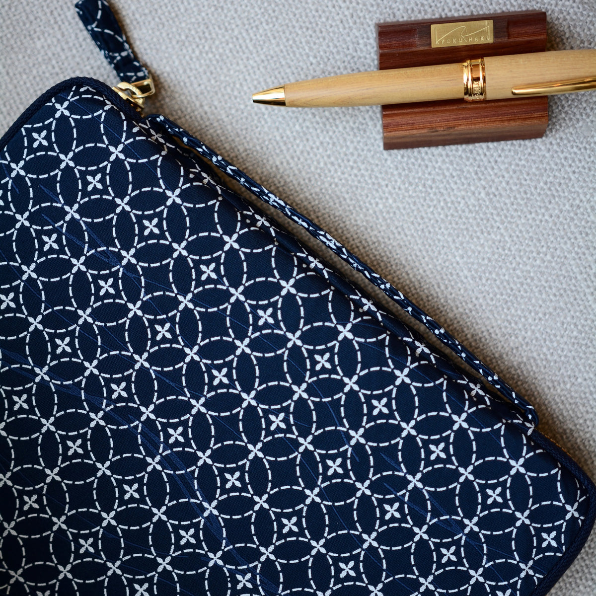 Navy blue pouch with white geometric pattern, gold pen, and wooden box on gray surface
