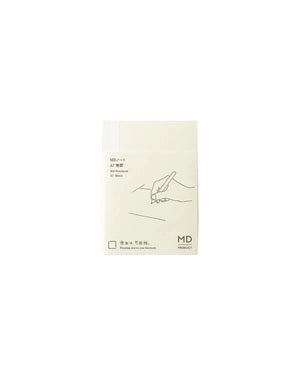A minimalist cream-colored notebook or journal with a simple line drawing of a hand holding a pen, shown against a light gray background. The cover features black text and the 'MD' brand logo.