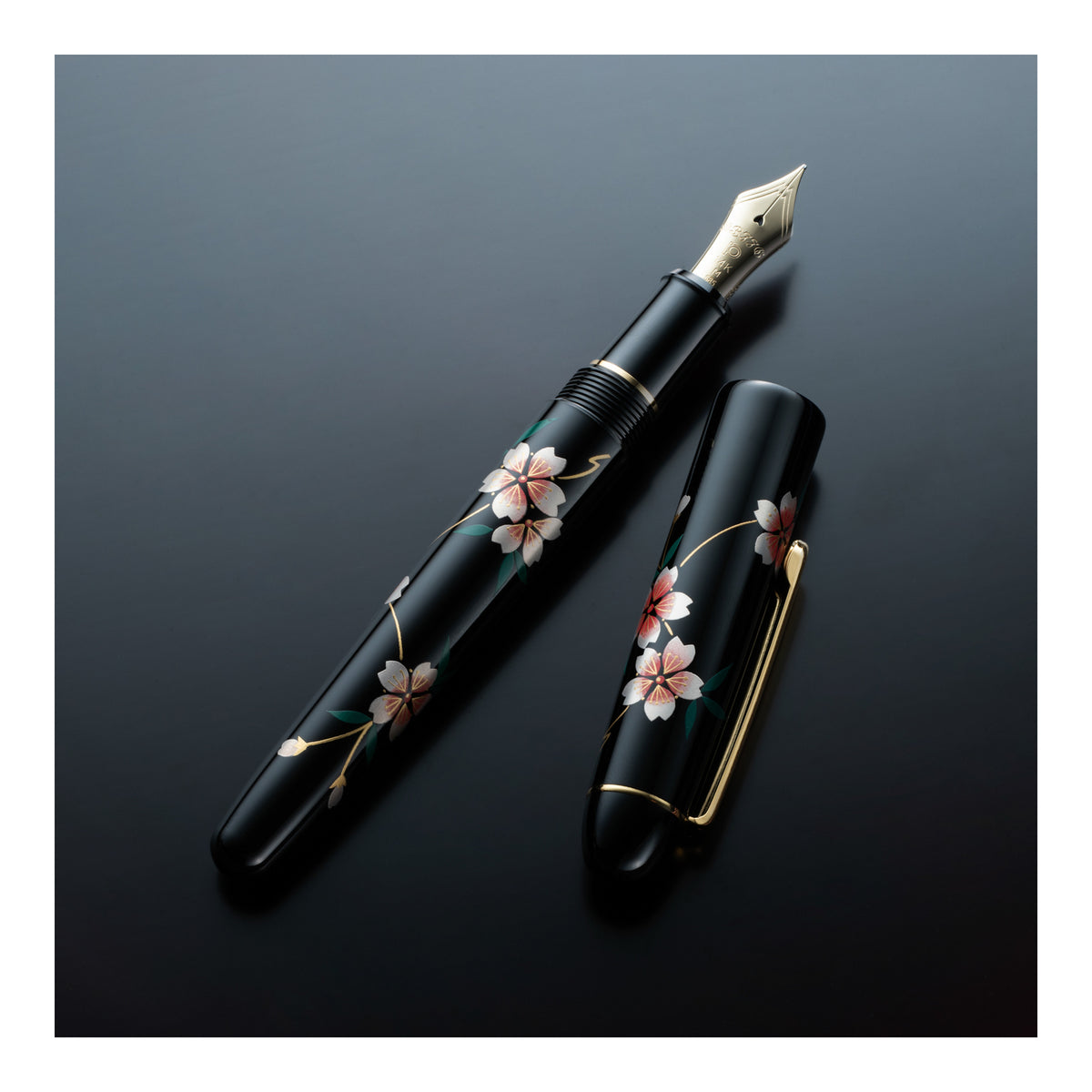 A black fountain pen and matching cap with hand-painted cherry blossom motifs, displayed on a dark reflective surface.