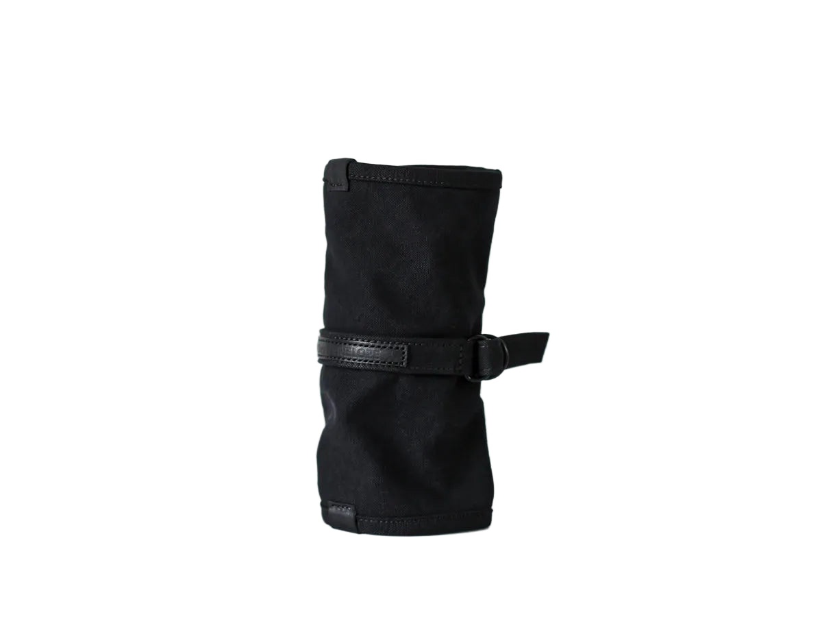 A black canvas wrist strap tool roll with a black leather strap and buckle, standing upright on a white surface against a white background. nomado store