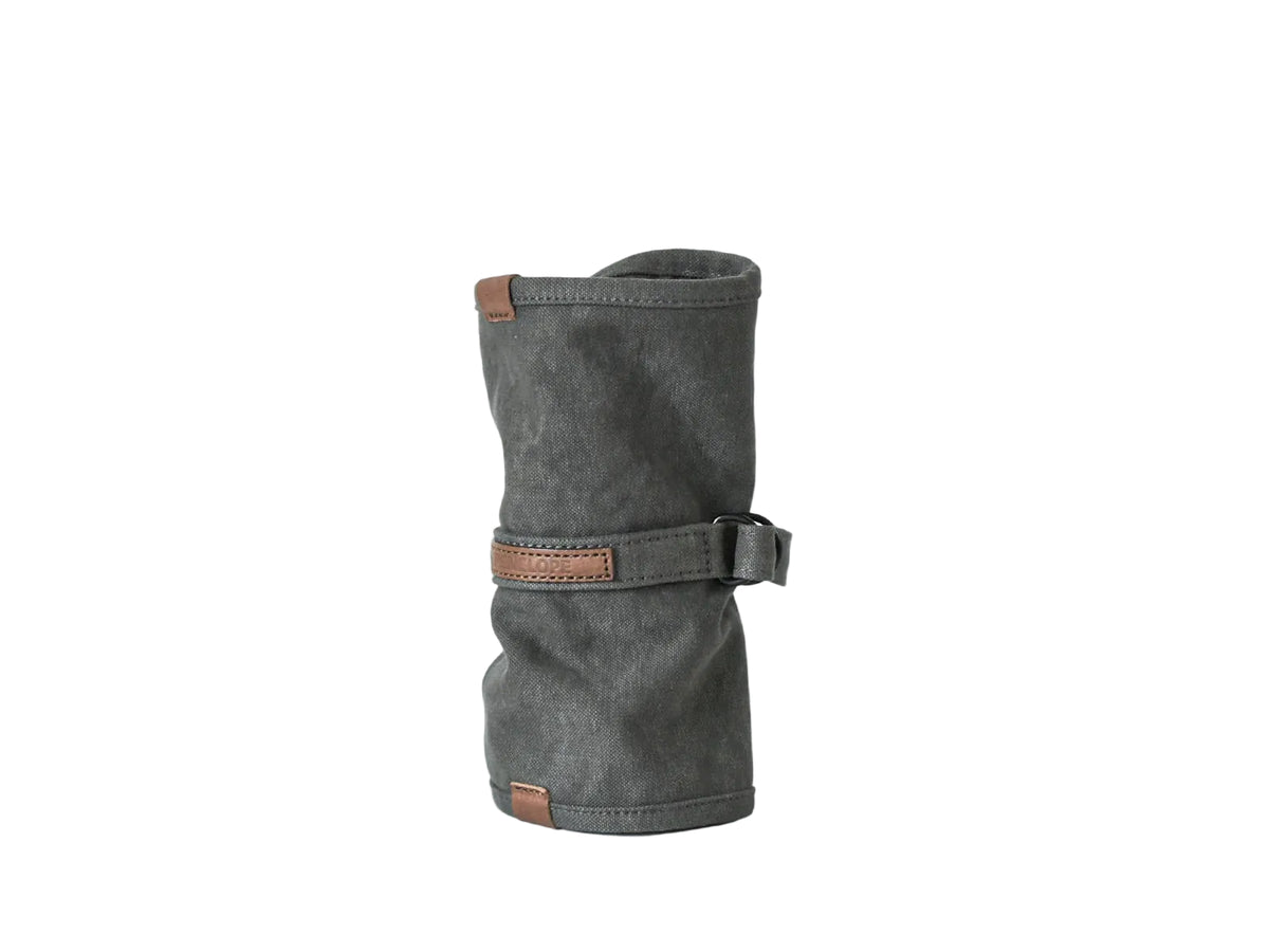 A dark gray canvas sleeve or pouch with brown leather trim and a strap closure, standing upright on a clean white studio background.  nomado store