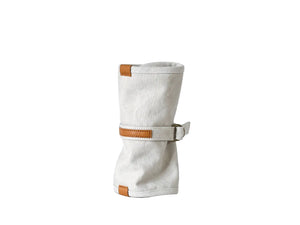 A light beige canvas sleeve with tan leather trim and a matching leather strap closure, standing upright on a white surface against a white background.