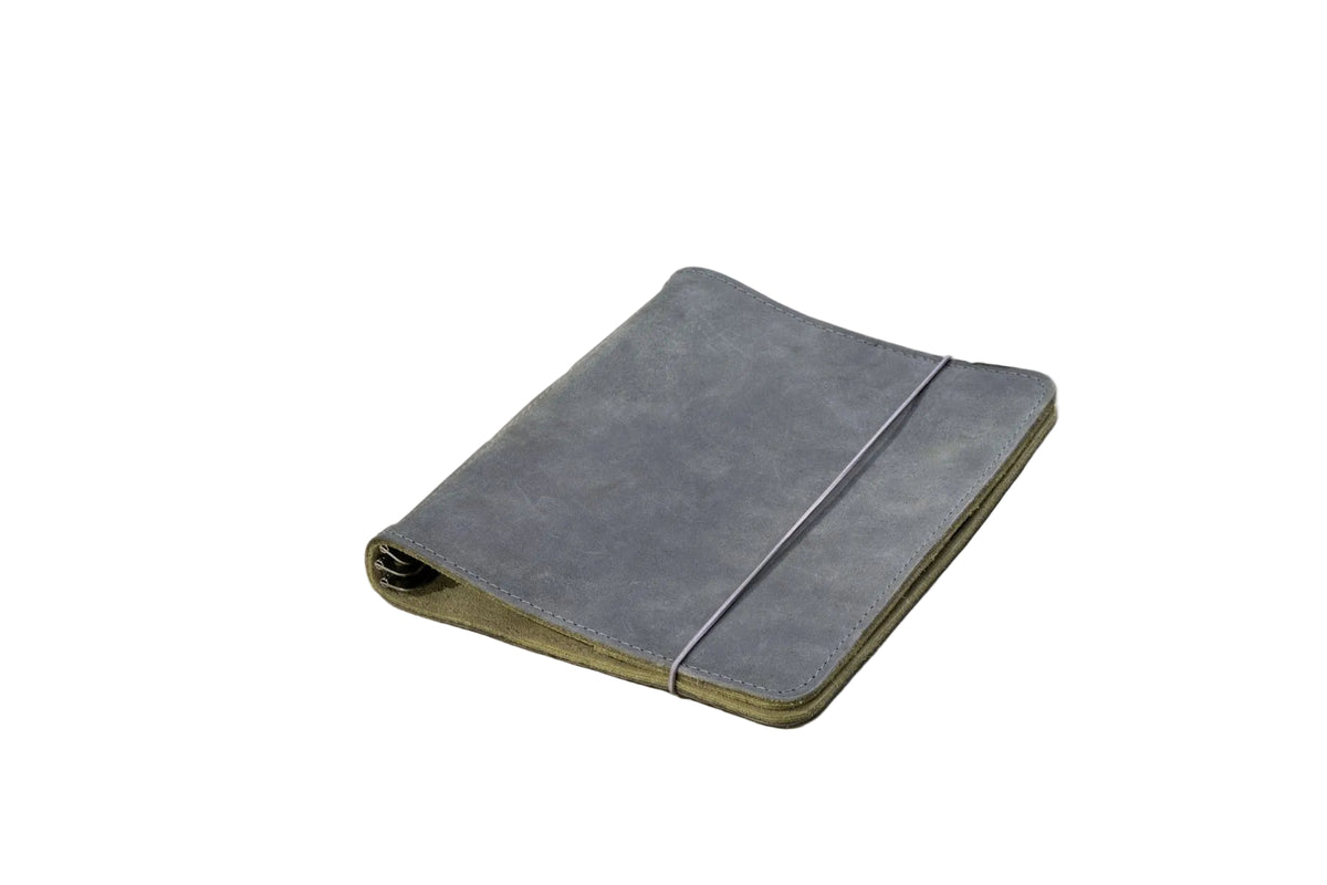 A closed gray suede or microfiber planner or notebook cover with a thin elastic band closure, resting on a light gray surface.
