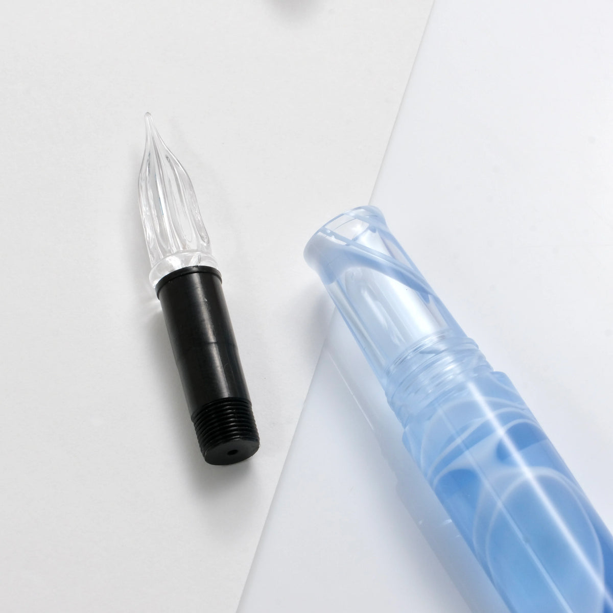 A close-up of a pen's nib and cartridge components on a clean white background. The nib is black with a clear ribbed tip, and the translucent blue cartridge is partially visible.