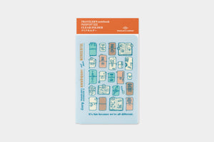 A packaged clear travel notebook folder shown on a light gray background. The top header is orange and reads 'TRAVELERS notebook CLEAR HOLDER,' with a blue card below featuring illustrated travel-themed icons in pastel blue, peach, and orange.